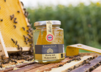 Dieses Bild zeigt einen Honig mit Wabe der Imkerei BienenStich aus Manhartsbrunn, Österreich. BienenStich ist ein kleiner Familienbetrieb in der Nähe von Wien und es wird in der Imkerei hochwertiger BIO-Honig hergestellt.